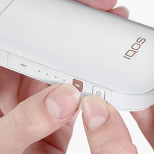 Sõrmed suruvad IQOS 2.4 PLUS-seadme nuppe